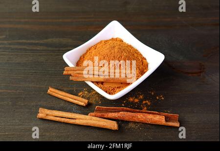 Gemahlenes Zimtpulver mit Stöcken in einer weißen Schüssel Dunkelbrauner Holzhintergrund Stockfoto