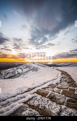 Atemberaubender goldener Sonnenaufgang über dem schneebedeckten Berg Mam Tor in der Landschaft des Derbyshire Peak District, atemberaubende Wolkenlandschaft. Winterszene Stockfoto
