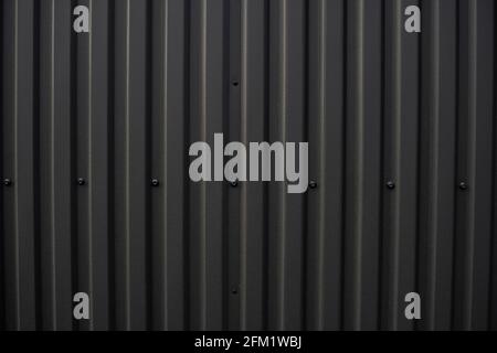 Schwarzes Wellblech, das als Fassade eines Lagers oder einer Fabrik verwendet wird. Textur einer nahtlosen Wellblech-Aluminium-Fassade aus Zinkblech Stockfoto