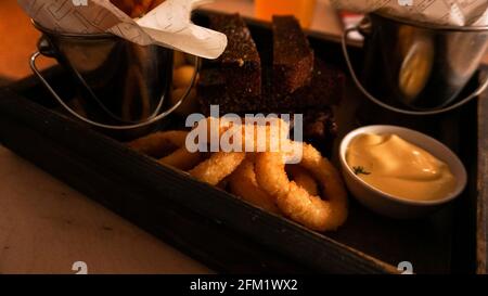 Bierset mit Snacks auf einem Holztablett. Zwiebelringe und Saucen. Snack für Freunde in einer Brasserie Stockfoto