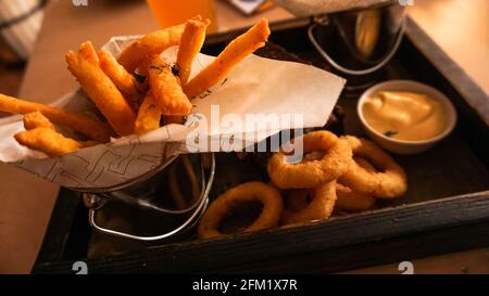 Bier-Set mit Snacks auf einem Holztablett. Zwiebelringe, Käsestäbe. Saucen. Snack für Freunde in einer Brasserie Stockfoto