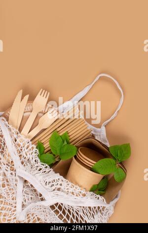 Vertikale Komposition mit umweltfreundlichem Geschirr - Kraftpapier-Food-Becher Und Behälter mit Holzbesteck in Baumwollnetzbeutel auf kraftpapier Stockfoto