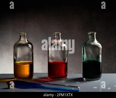 Drei Gläser mit dem verschiedenfarbigen Getränk im Inneren. Gelb, rot und grün. Reagenzglas mit blauem Getränk vorne. Stockfoto