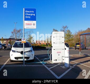 Ein Elektroauto, das mit einer Ladestelle in einem Supermarkt-Parkplatz in Sprowston, Norfolk, England, Großbritannien, verbunden ist. Stockfoto