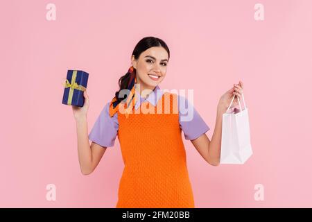 Zufrieden Frau zeigt Geschenkbox und Einkaufstasche isoliert auf Rosa Stockfoto