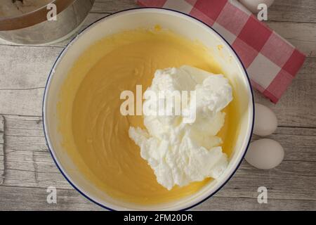 Frisch gerührter Kuchenteig mit geschlagenem Eiweiß in einer Schüssel auf rustikalem Holztisch-Hintergrund. Ansicht von oben Stockfoto