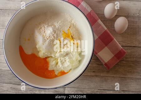 Zutaten für eine Käsekuchen-Füllung in einer weißen Emaille-Schüssel Von oben auf Holztisch Hintergrund Stockfoto