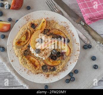 Lecker frisch gebackene glutenfreie Haferflocken Pfannkuchen mit Äpfeln gebacken Und Heidelbeeren und gekrönt mit proteinreichem Quark und Zimt Stockfoto