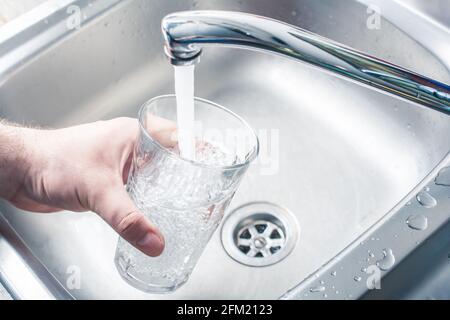 Hand Halten Trinkglas Über Küchenspüle Füllen Es Mit Wasser Streaming Aus Wasserhahn Stockfoto