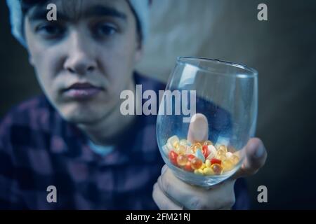 Trauriger Kerl mit einem Glas Pillen und Medikamenten. Behandlung und Prävention in Quarantäne. Kranker Mann in einem karierten Hemd. Weinglas mit Vitaminen. Stockfoto