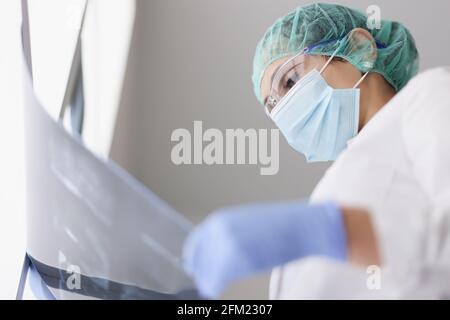 Ein Arzt, der eine Schutzmaske und Handschuhe trägt, untersucht ein Röntgenbild Stockfoto