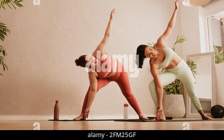 Zwei Frauen machen Yoga im Fitness Studio. Fitness-Frauen machen Triangle Yoga Pose, Trikonasana im Fitnessstudio. Stockfoto