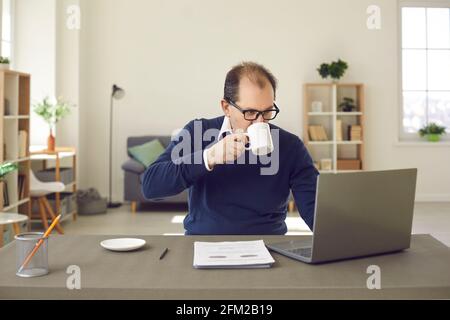 Reifer kaukasischer Mann in einer Brille, der an einem Laptop arbeitet und Kaffee trinkt Zu Hause Stockfoto