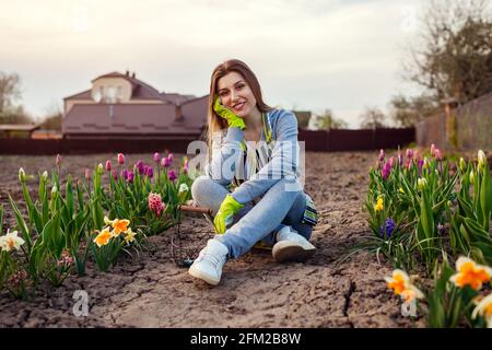 Gärtner, der sich unter frischen Tulpen, Narzissen und Hyazinthen im Frühlingsgarten entspannt. Glückliche Frau genießt bunte Blumen Stockfoto