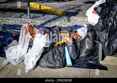 Obdachloser schwarzer Mann, in Plastik gewickelt, schläft auf dem Bürgersteig, Vancouver, British Columbia, Kanada Stockfoto