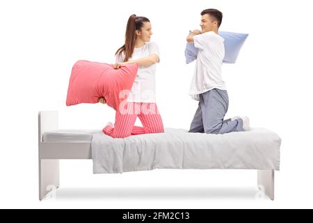 Junge Männer und Frauen im Schlafanzug kämpfen mit Kopfkissen Ein Bett auf weißem Hintergrund isoliert Stockfoto