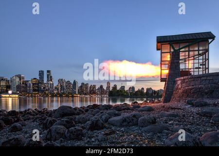 Vancouver Nine O'Clock Gun feuert während der blauen Stunde im Dunkeln mit Stadtbild im Hintergrund, Stanley Park, Vancouver, BC, Kanada. Stockfoto