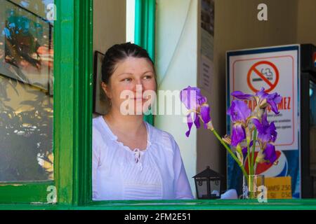 Gokceada, Canakkale - Türkei - Mai 06 2013: Junge türkin mit weißem Hemd, sitzt in einem Café, blickt aus einem grünen Fenster, lila Blumen i Stockfoto