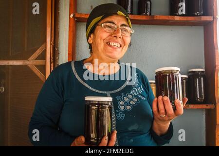 Gokceada, Canakkale - Türkei - 07 2013. Mai: Eine türkische Bäuerin hält zwei Gläser Marmelade in ihren Händen und lächelt, Tepekoy Stockfoto