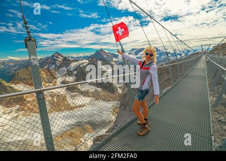 Frau mit Schweizer Flagge auf Titlis Klippe gehen Hängebrücke. Gipfel des Titlis mit Gletscher in den Uri Alpen. Aussichtspunkt 3028 m in den Kantonen Stockfoto