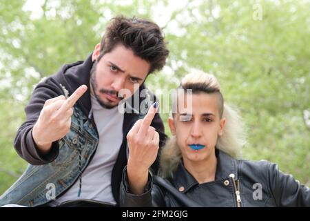 Ein junges Punk-Paar, das den Vogel in einem Park an die Kamera dreht. Rock and Roll Lifestyle. Stockfoto