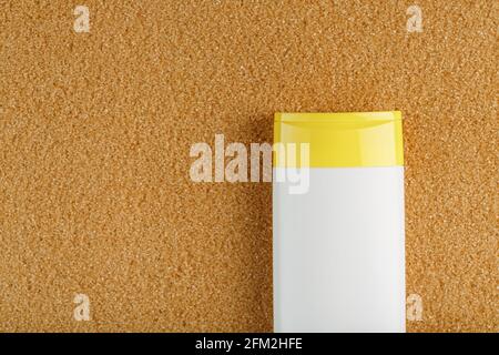 Sonnencreme in einer weißen Flasche mit einer gelben Kappe auf dem goldenen Sand. Freier Speicherplatz und Platz für Text, Draufsicht Stockfoto
