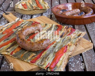 Ein Stück Coca de recte, ein typisch katalanischer pizzinoähnlicher herzhafter Kuchen, der mit gegrillten Auberginen und rotem Pfeffer und Schweinewurst auf einem rustikalen Holzkohlensäurehaus zubereitet wird Stockfoto