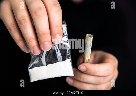 Drogenhändler, der Drogen in einer Plastiktüte, Kokain, Heroin, Speed oder andere Drogen auf dunkelschwarzem Hintergrund gibt, sucht, Drogen, klobig, kriminelles Konzept Stockfoto