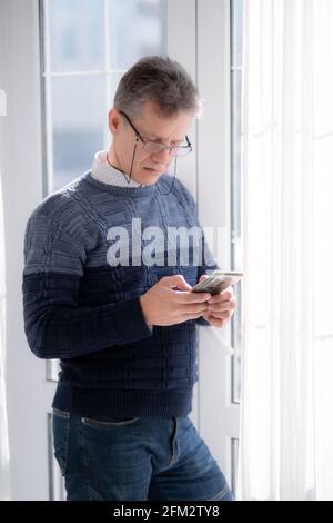 Ein Mann Geschäftsmann mit Brille steht im Hintergrund von Ein Fenster mit einem Telefon Stockfoto