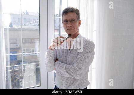 Ein Mann Geschäftsmann in einem weißen Hemd und einer Brille mit Ein Telefon steht am Fenster Stockfoto