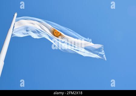 Argentinische Flagge, die an einem sonnigen Tag auf einem Fahnenmast gegen einen blauen Himmel fliegt. Patriotisches Symbol Argentiniens Stockfoto