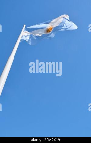 Argentinische Flagge, die an einem sonnigen Tag auf einem Fahnenmast gegen einen blauen Himmel fliegt. Patriotisches Symbol Argentiniens Stockfoto