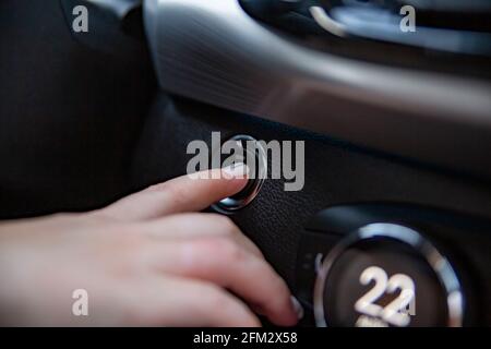 Fahrer Hand Finger drückt die Start-Stopp-Taste in einem modernen Auto. Nahaufnahme. Kein Gesicht. Schlüssellose Option im Auto. Selektiver Fokus Stockfoto