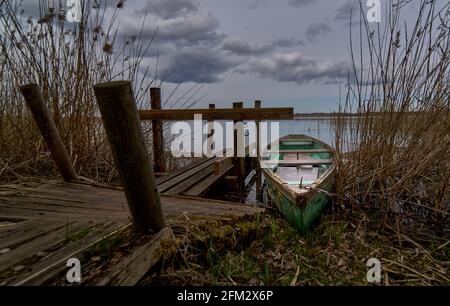 Ein kleines grünes Boot schwimmt auf dem See in der Nähe der pier Stockfoto