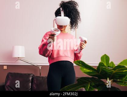 Frau im Sweatshirt mit einem VR-Set, während sie im Stehen steht Wohnzimmer Stockfoto
