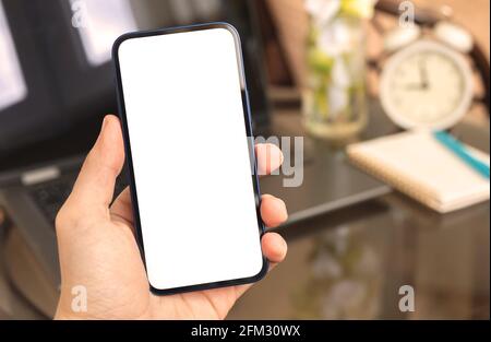 Mann, der Smartphone-Modell auf dem Hintergrund des Laptops verwendet, Heiminterieur mit Wecker und Heimanlage, Kopierraum Stockfoto