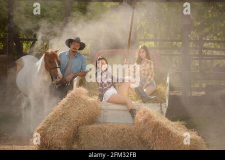 Zwei Frauen, die auf einem Lastwagen sitzen, und ein Mann, der mit einem Pferd auf einer Farm in Thailand steht Stockfoto