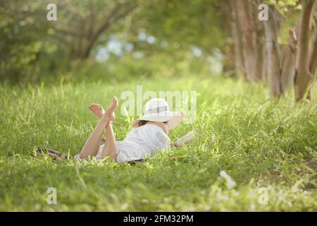 Rückansicht einer Frau, die im Sommer auf einer Wiese liegt und ein Buch liest, Thailand Stockfoto