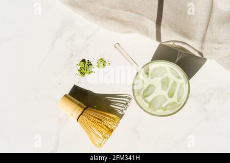 Blick von oben auf ein gekühltes Matcha-Getränk mit grünem Tee neben Matcha-Pulver, Bambusbesen und Löffel Stockfoto