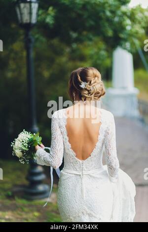 Braut in weißem Kleid mit einem Rosenstrauß am Zurück Stockfoto