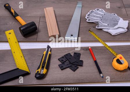 Ausrüstung oder Werkzeuge zum Einbau von Laminatboden. Hammer, Brechstange, Distanzstücke, Schneider, Schutzhandschuhe und Klebeband messen auf dem Laminatboden. Selektive Stockfoto