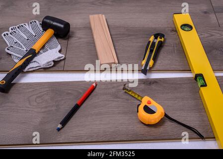 Ausrüstung oder Werkzeuge zum Einbau von Laminatboden. Gummihammer, Schneider, Schutzhandschuhe, Bleistift, Wasserwaage-Werkzeug und Klebeband messen auf dem Laminatflo Stockfoto