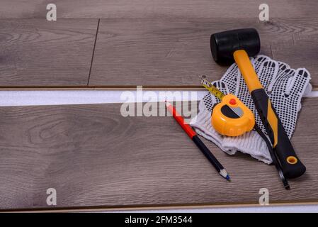 Ausrüstung oder Werkzeuge zum Einbau von Laminatboden. Gummihammer, Schutzhandschuhe, Bleistift und Klebeband messen auf dem Laminatboden mit Platz für die Kopie von tex Stockfoto