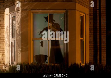 Halloween Fenster Silhouette Dekoration: Eine Hexe fügt eine Ratte oder Maus zu ihrem Kessel. Die Straße draußen spiegelt sich im Fenster wider. Stockfoto