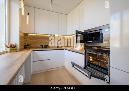 Moderne weiße und beige Holzküche mit Backofen geöffnet Stockfoto