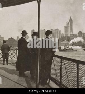 Singer Tower und riesige Bürogebäude, von der Fähre aus gesehen in North River, New York, USA - drei Männer auf der Fähre, die Boote und New York City in der Ferne ansahen, um 1908 Stockfoto