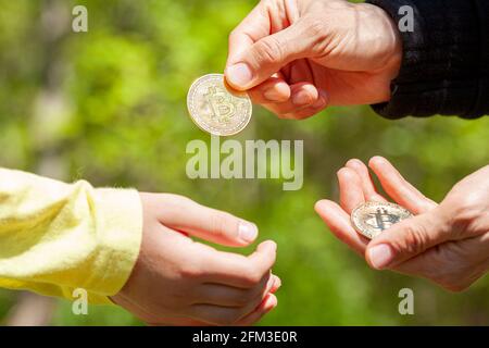 Ein Kind bittet um Taschengeld und seine Eltern geben als Antwort eine Bitcoin-Münze. Konzeptbild in Familieneinstellung zur Verwendung von Kryptowährung in d Stockfoto