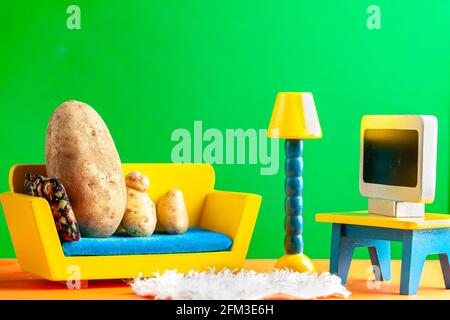 Ein skurriles metaphorisches Konzeptbild, das eine Kartoffelfamilie zeigt, die auf einer Couch liegt und im Wohnzimmer Fernsehen sieht. Bild für Couch Potato, obesi Stockfoto