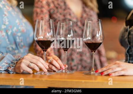 Nahaufnahme der Hände unbekannter Frauen, die eine Brille halten Von Rotwein auf dem Tisch Stockfoto