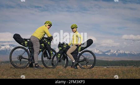 Der Mann und die Frau reisen auf gemischtem Terrain mit Bikepacking. Die beiden Personen reisen mit Fahrradtaschen. Schneebedeckte Berge. Stockfoto